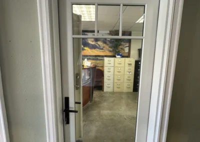 A modern glass door with a white frame, leading to an office space with filing cabinets and a scenic backdrop.