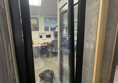 A black dog sleeps on a gray blanket inside an office, viewed through a sleek black window frame.