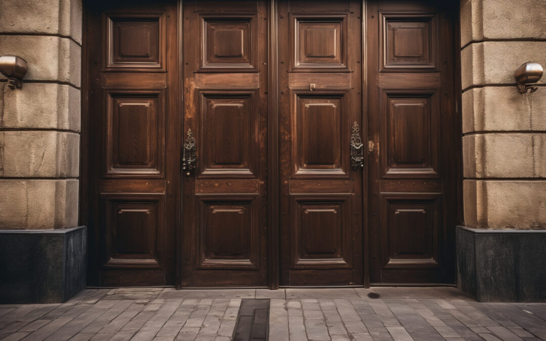 A grand set of ornate wooden double doors with detailed carvings and antique handles on a stone building facade.